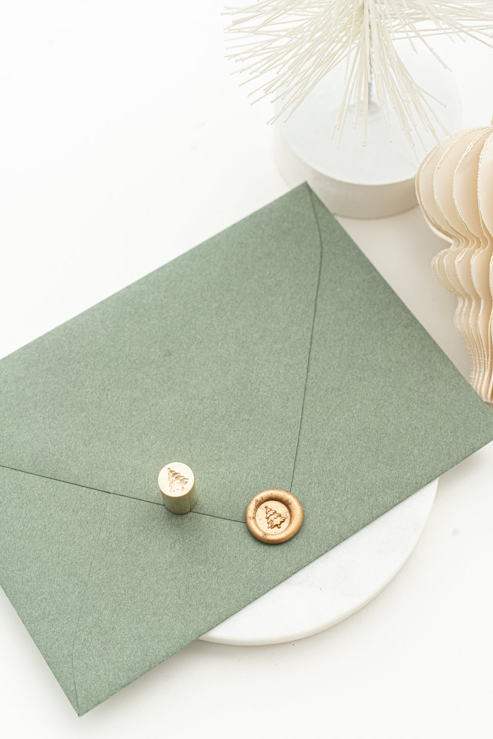 A wax steal stamp in gold of a 3d illustration of a Christmas Tree on a green envelope.