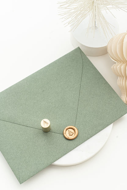 A wax steal stamp in gold of a 3d illustration of a Christmas Tree on a green envelope.