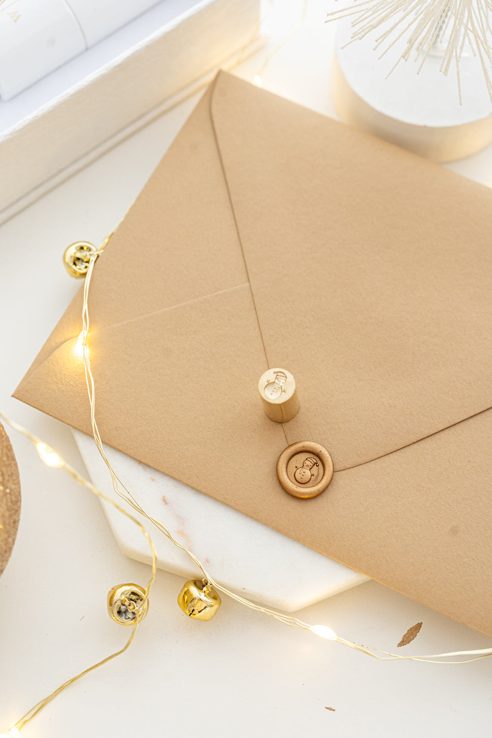 Festive mini wax seal stamp with snowman design in gold wax on a kraft envelope, part of Written Word Calligraphy’s Holiday Collection.