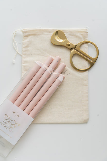 Set of blush sealing wax sticks with a pair of scissors and a drawstring bag on a white background