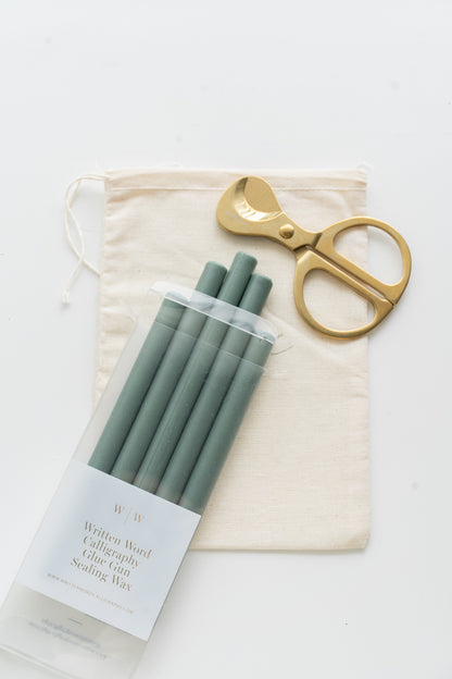 Set of green sealing wax sticks with a pair of scissors and a drawstring bag on a white background