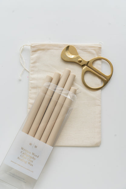 Set of beige sealing wax sticks with a pair of scissors and a drawstring bag on a white background