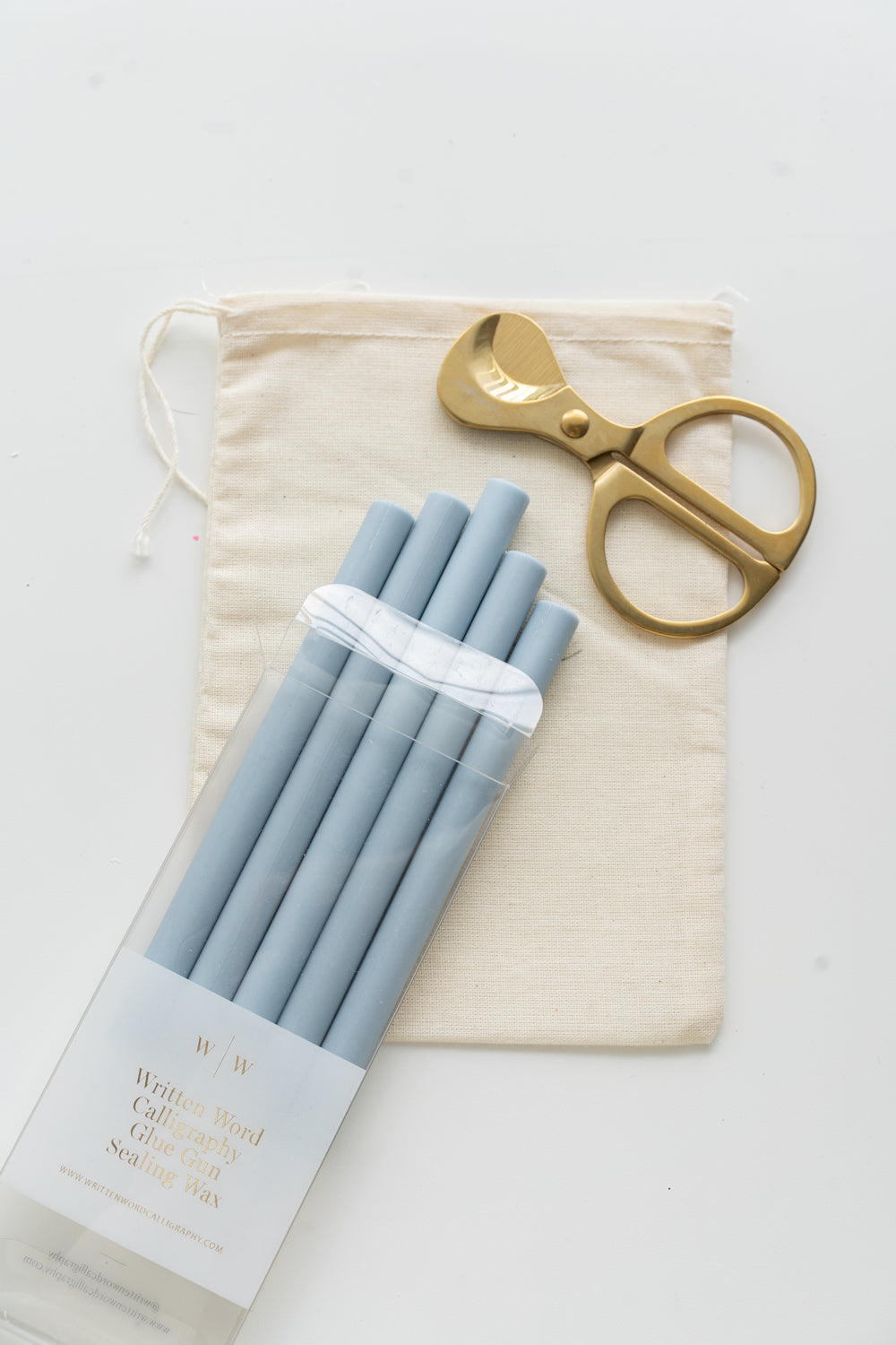 Set of blue sealing wax sticks with a pair of scissors and a drawstring bag on a white background