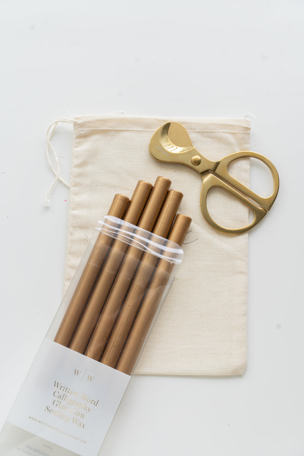 Set of gold sealing wax sticks with a pair of scissors and a drawstring bag on a white background