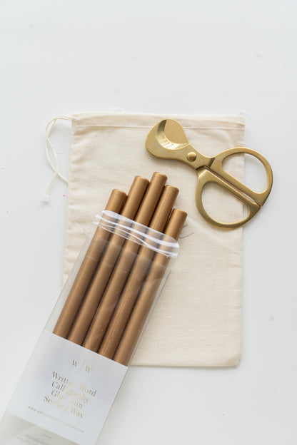 Set of gold sealing wax sticks with a pair of scissors and a drawstring bag on a white background