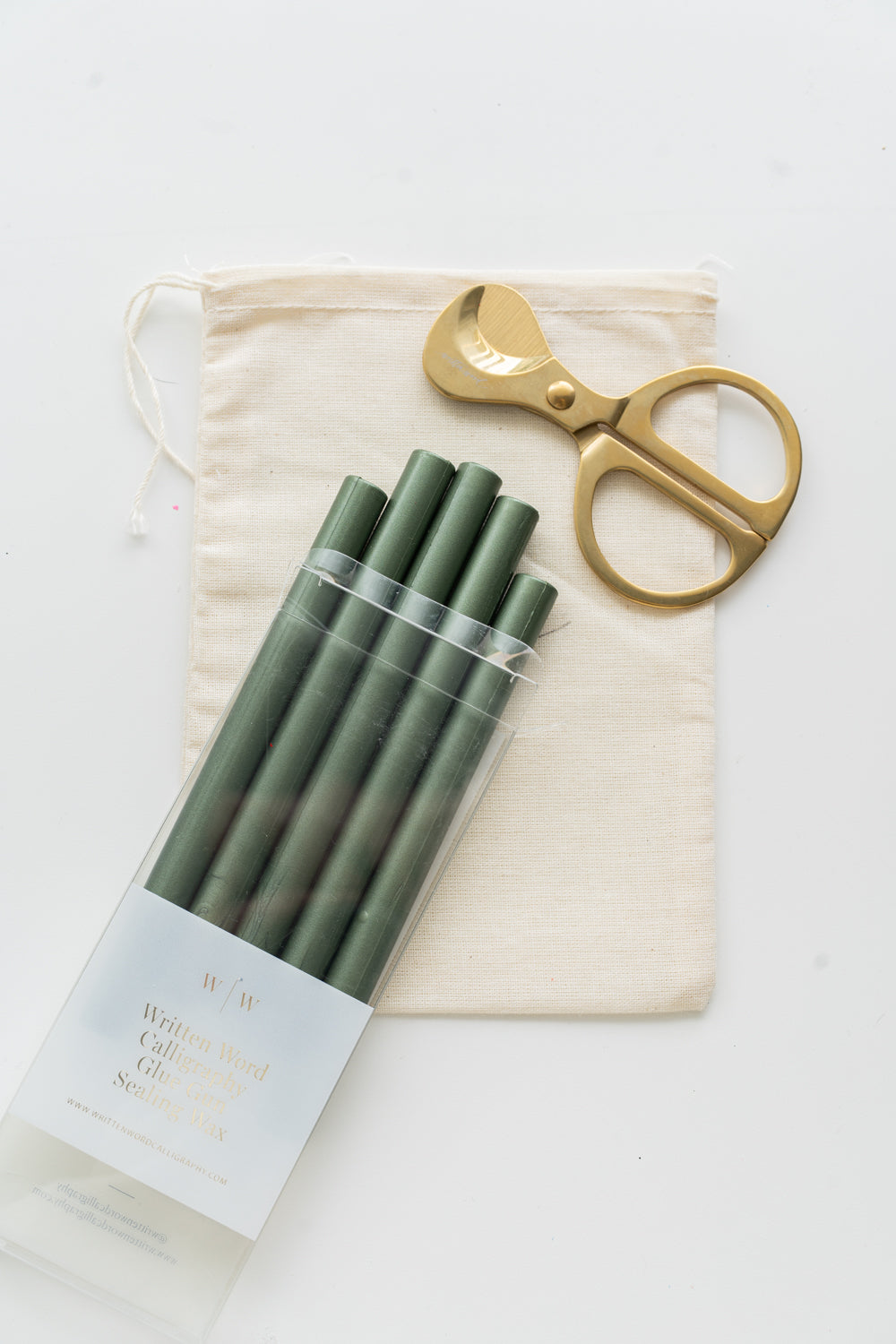 Set of emerald sealing wax sticks with a pair of scissors and a drawstring bag on a white background