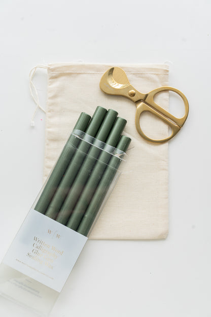 Set of emerald sealing wax sticks with a pair of scissors and a drawstring bag on a white background