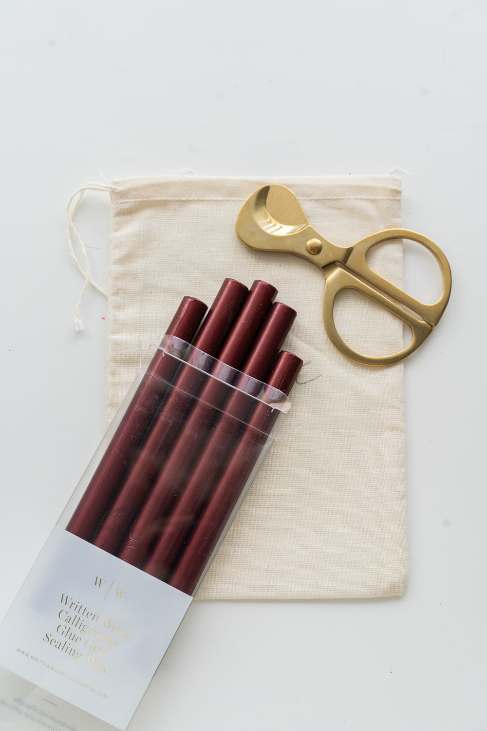 Set of crimson sealing wax sticks with a pair of scissors and a drawstring bag on a white background