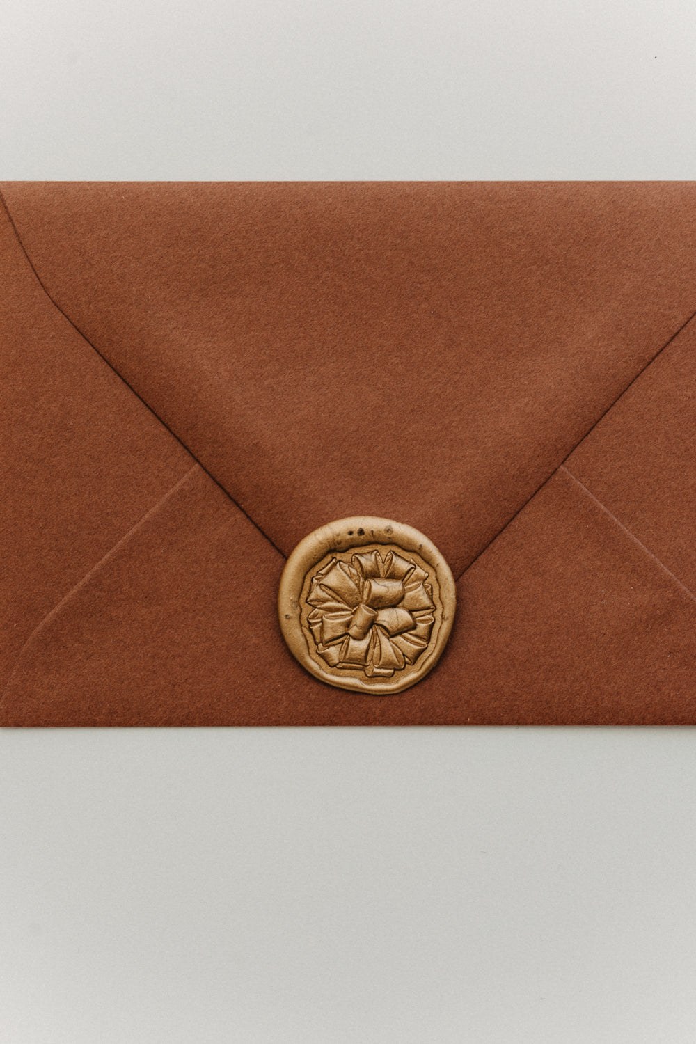 Rust terracotta envelope sealed with a gold gift bow wax seal, holiday stationery flat la