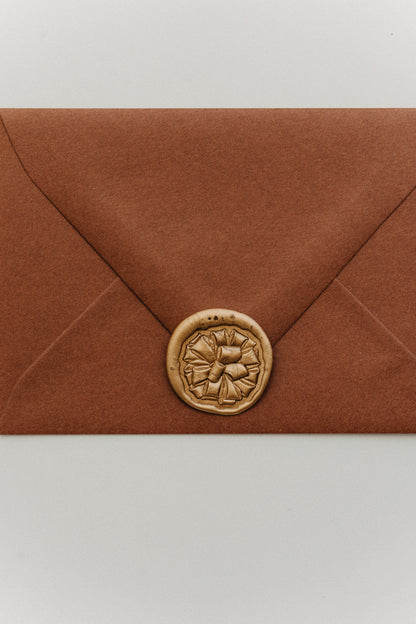 Rust terracotta envelope sealed with a gold gift bow wax seal, holiday stationery flat la