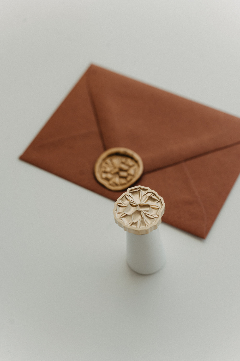 Gift bow wax seal stamp with gold wax seal on rust terracotta envelope for holiday cards