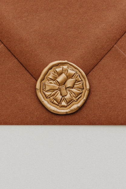 Close-up of gold gift bow wax seal on rust terracotta envelope flap, holiday card sealing