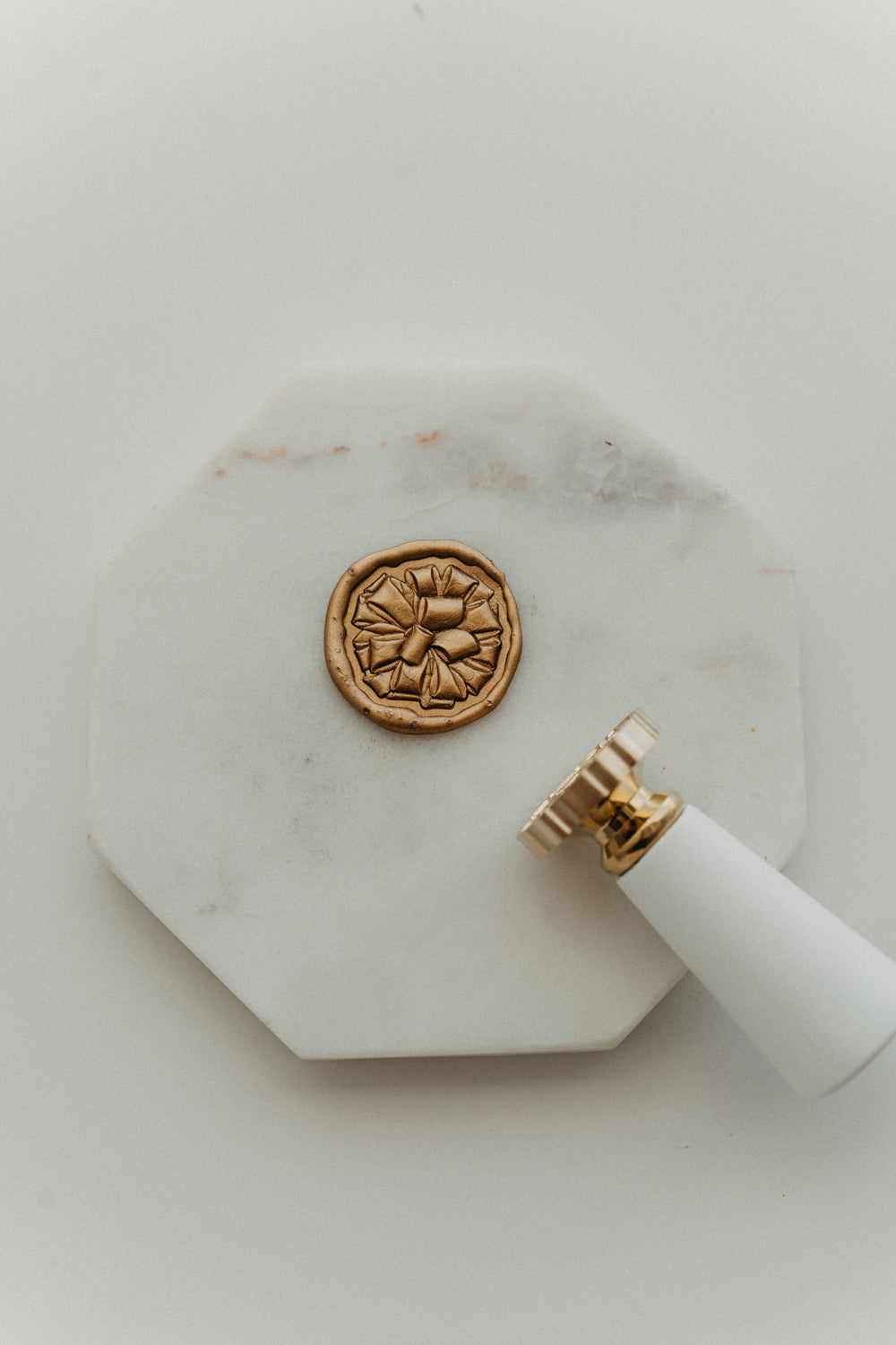 Gift bow wax seal stamp with gold wax seal on octagonal white marble tray, holiday stationery