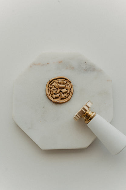 Gift bow wax seal stamp with gold wax seal on octagonal white marble tray, holiday stationery