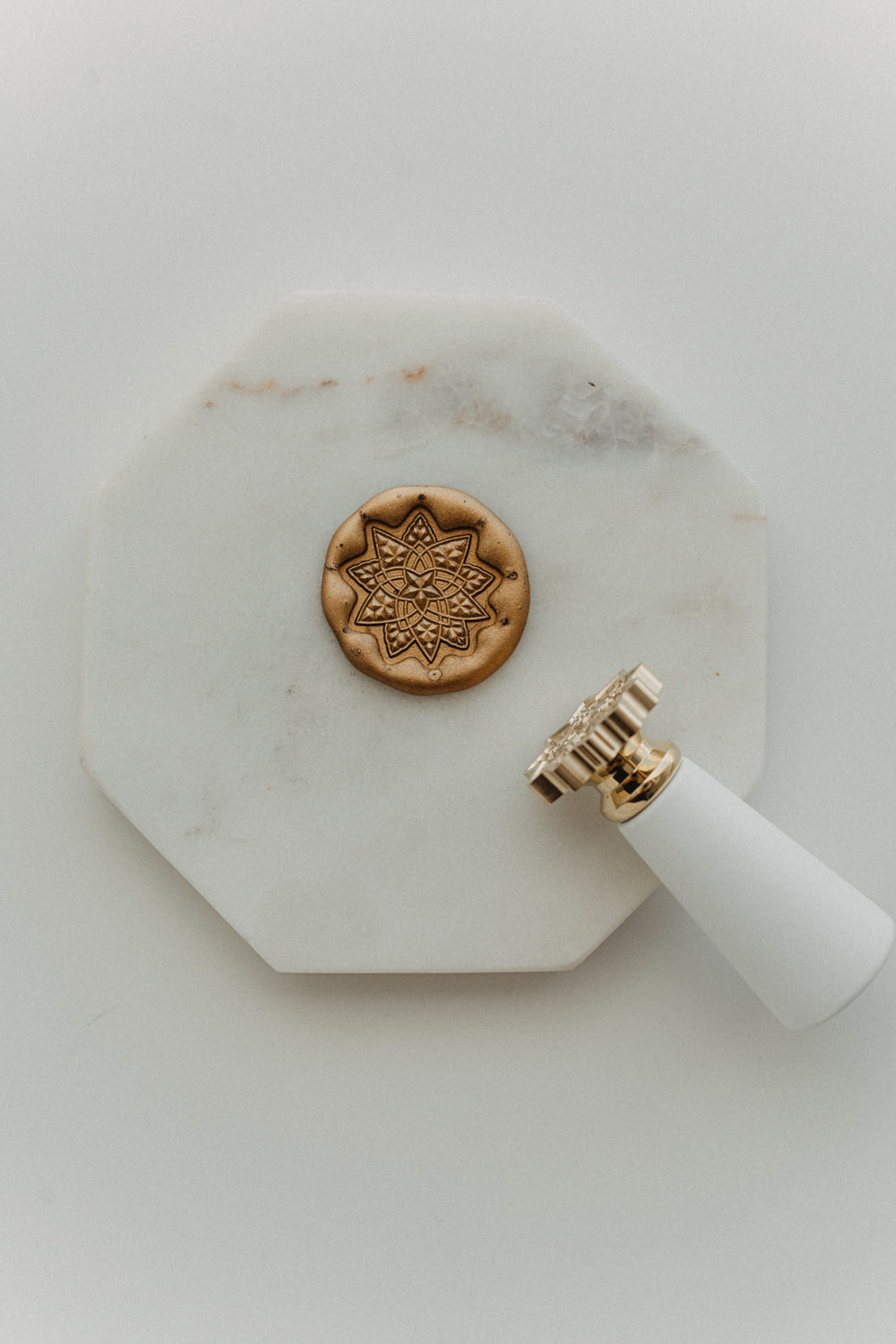 Gold geometric star wax seal and white-handled brass wax stamp displayed on a white marble tile.