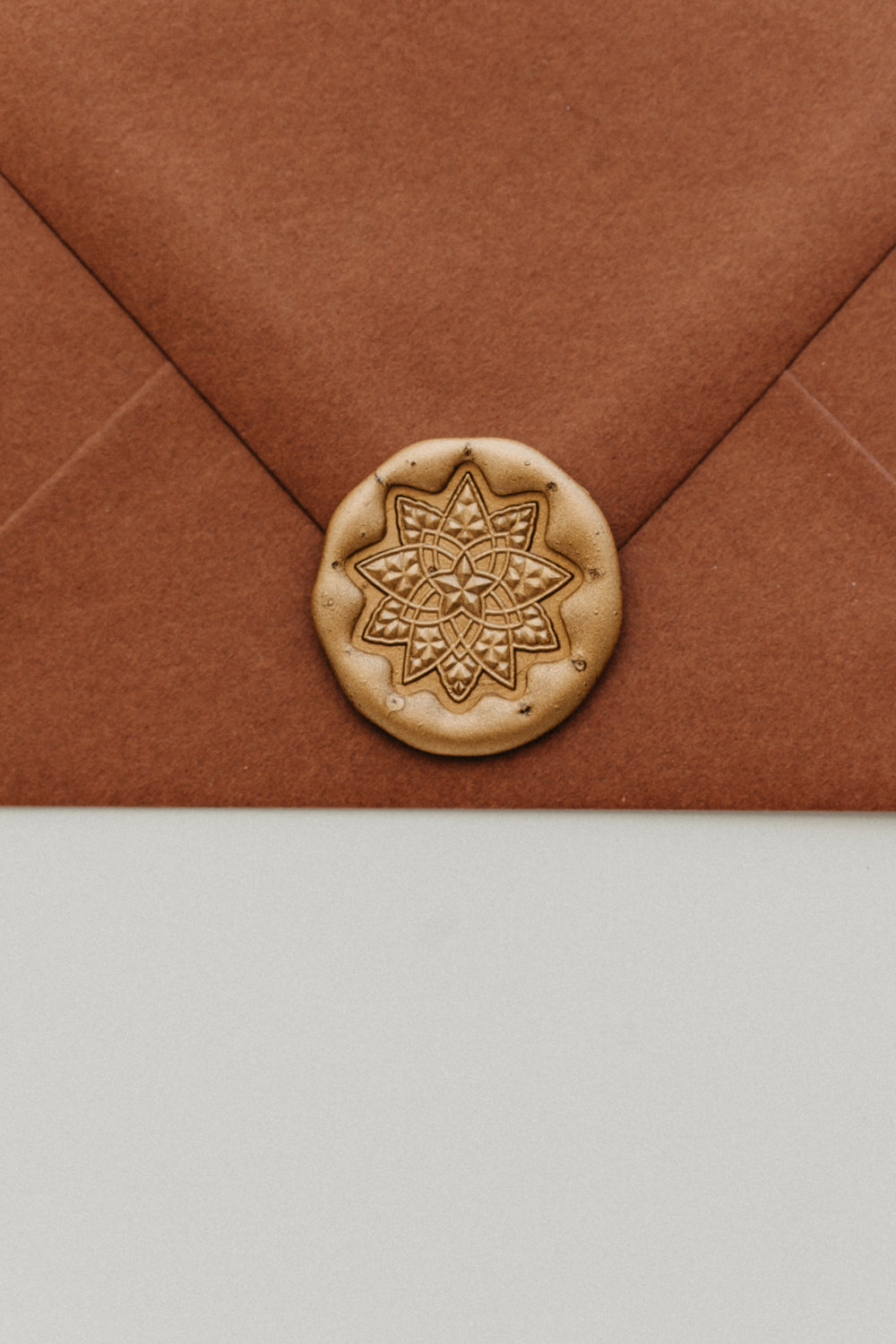 Close-up of a gold geometric star wax seal securing the flap of a warm brown envelope.