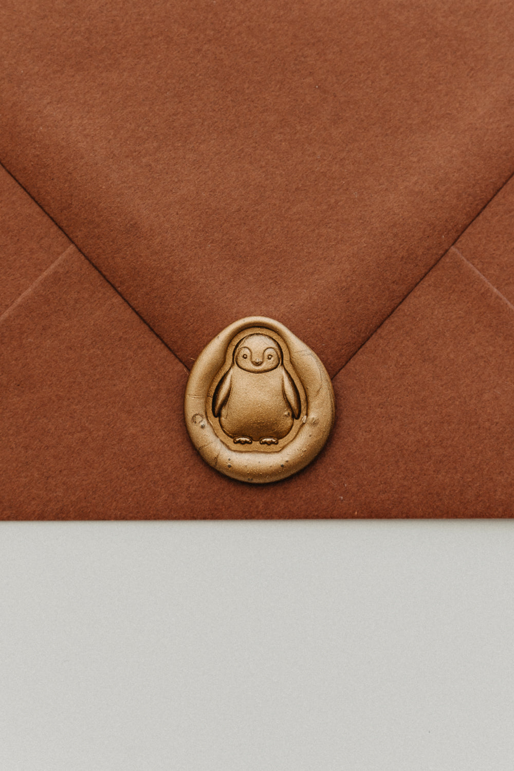 Close-up of a gold penguin wax seal securing the flap of a warm brown envelope.