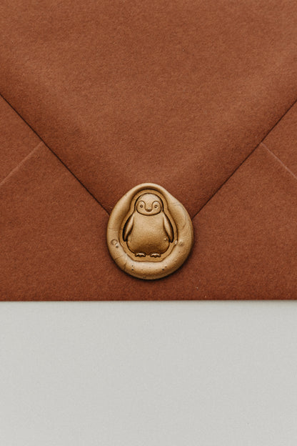 Close-up of a gold penguin wax seal securing the flap of a warm brown envelope.