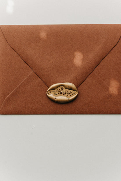 Gold “love” wax seal centered on the flap of a warm brown envelope.