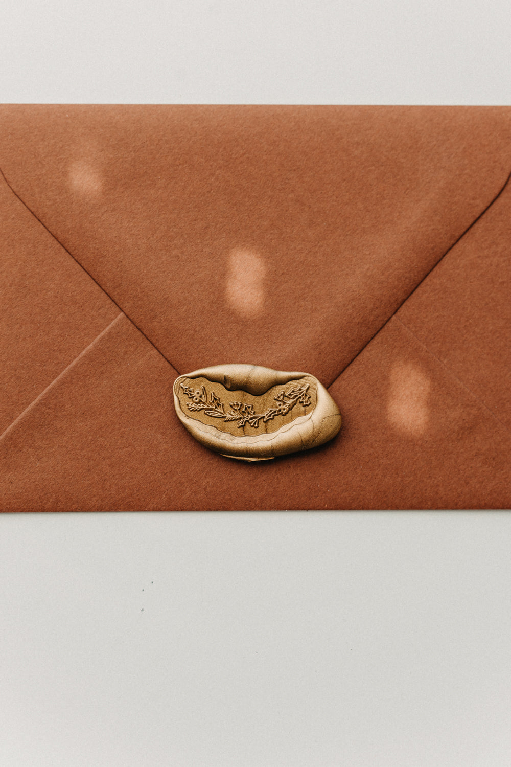 Metallic gold botanical garland wax seal securing a warm brown envelope.