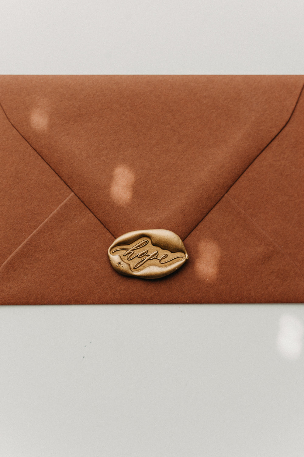Metallic gold “hope” wax seal securing a warm brown envelope, close-up stationery detail.