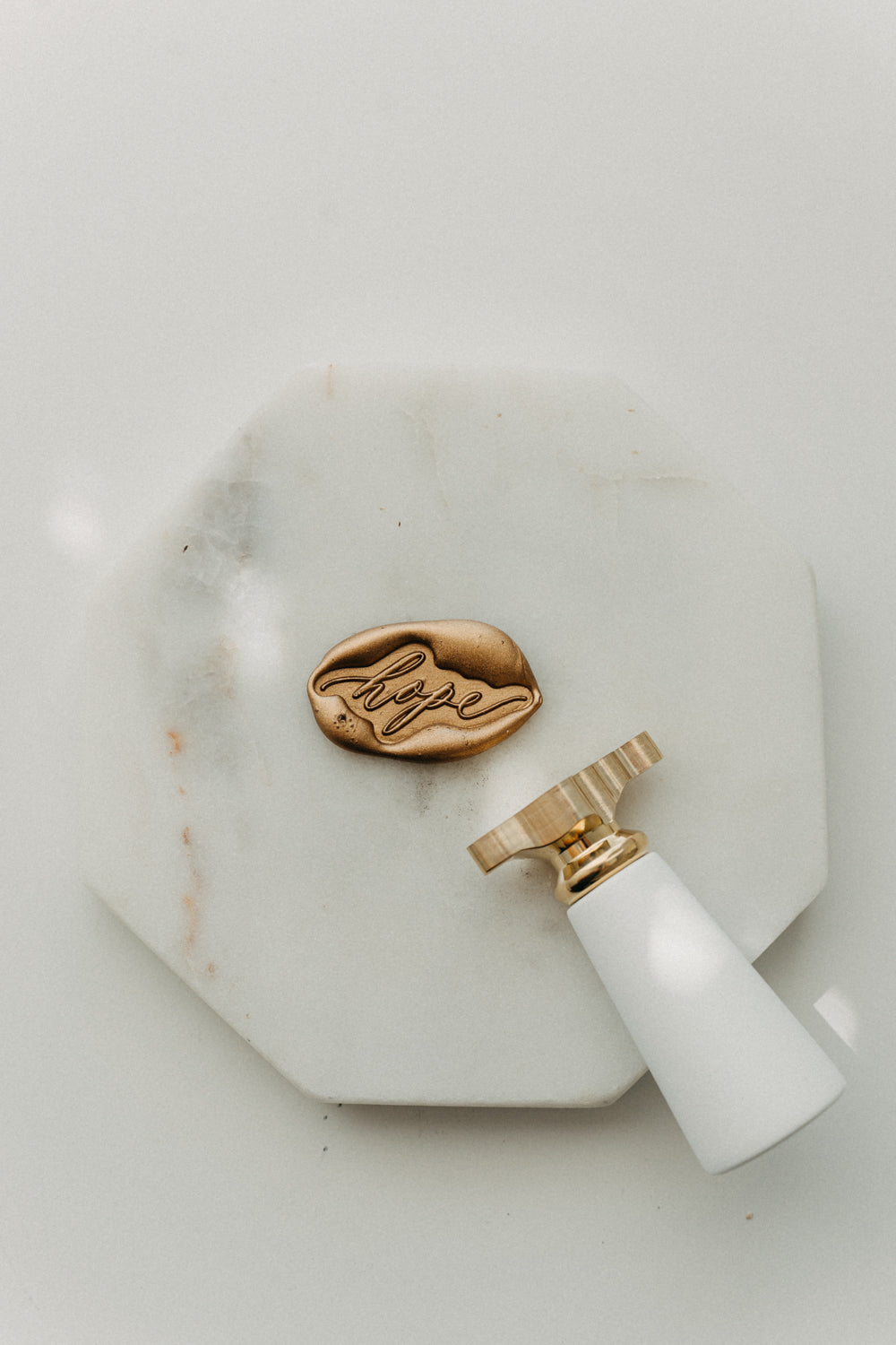 Gold “hope” wax seal and white-handled brass wax seal stamp on a white marble display tile.