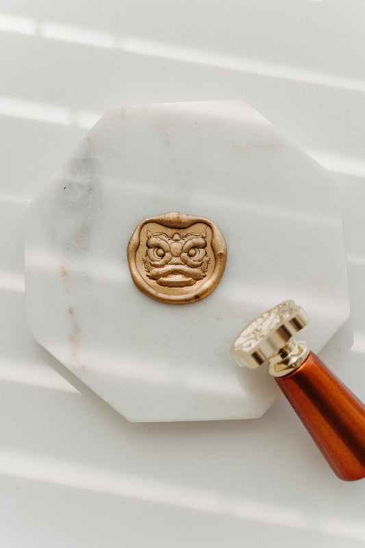 Detailed brass Lion Dance Head wax stamp head resting on marble stand