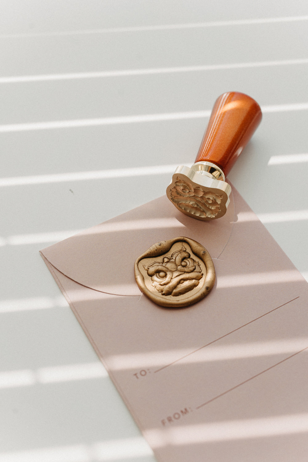 Lion Dance wax stamp onto pink envelope with melted gold wax