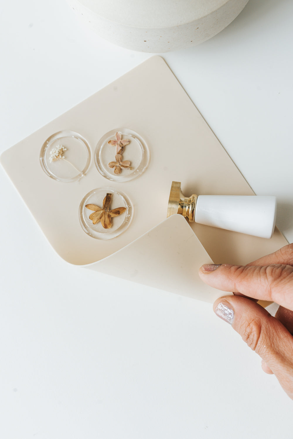 Clear wax seals with pressed flowers on beige silicone mat with wax seal stamp and hand lifting mat