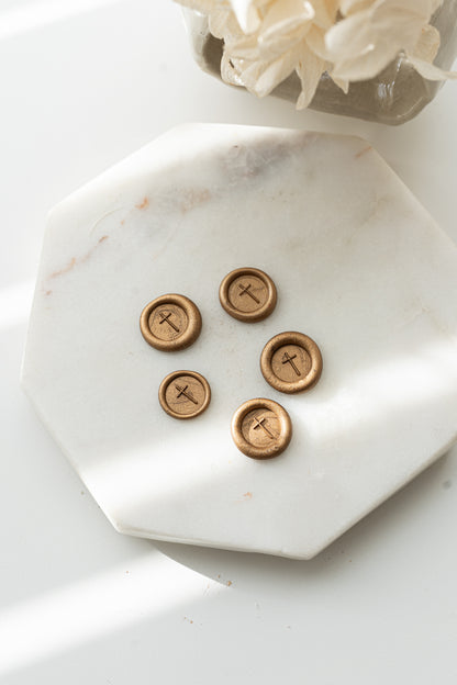 Five gold wax seals with a simple cross illustration arranged on a white marble tray, created with the limited edition 9mm diameter simple cross wax seal stamp