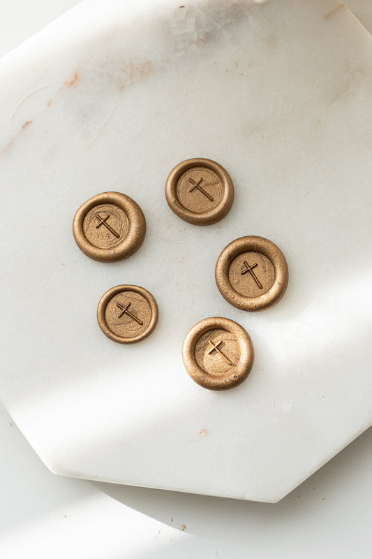 Close-up of gold sealing wax stamps with a cross design made using a mini wax seal stamp on a marble background.