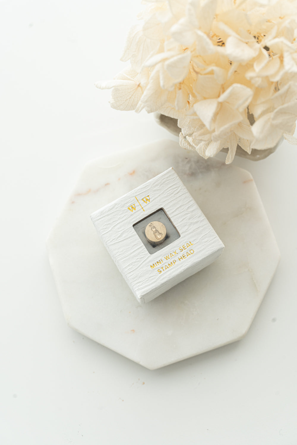 Mini wax seal stamp head in white textured box with gold foil text, styled with dried flowers on marble tray