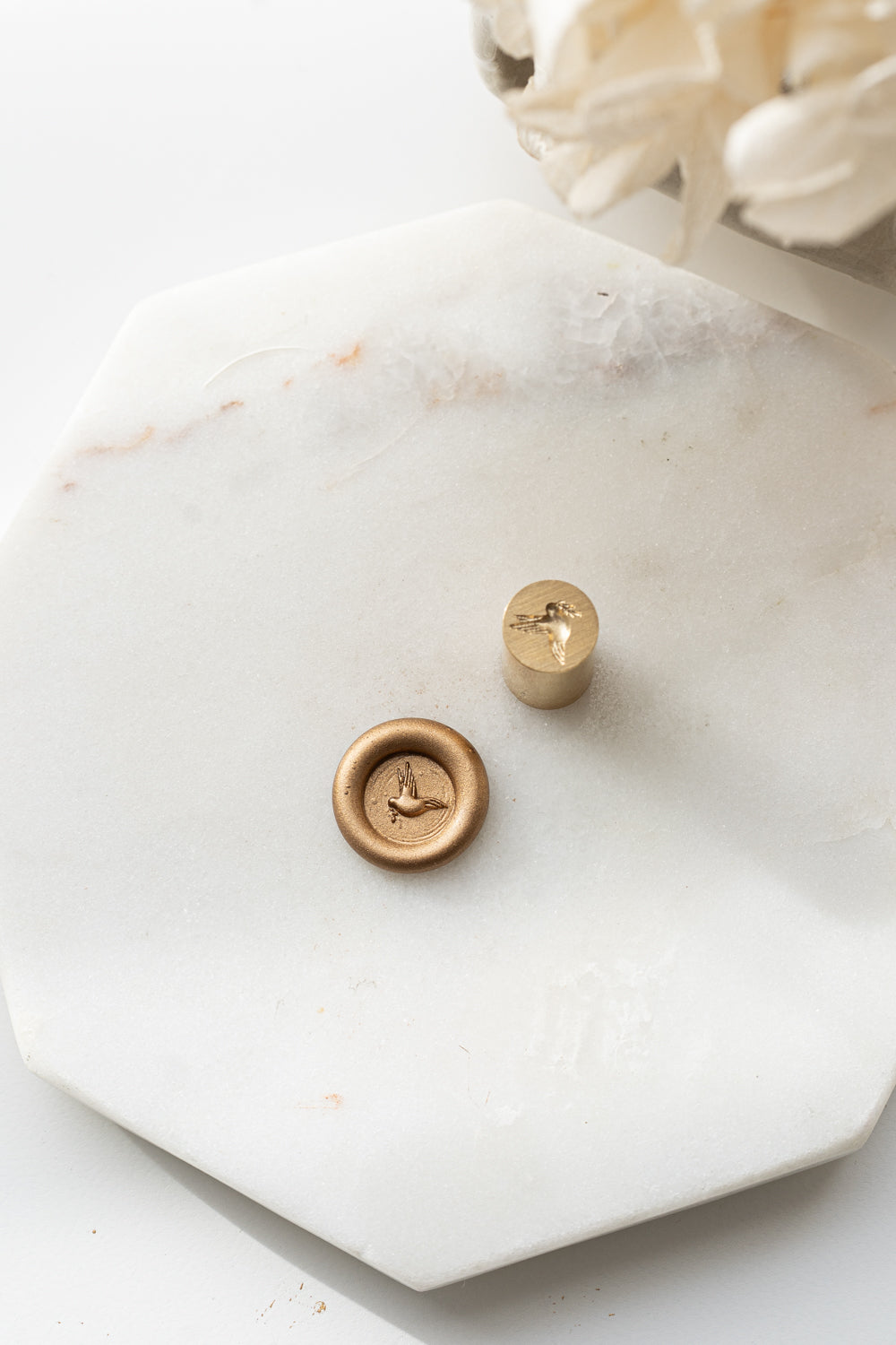 Brass mini wax seal stamp head with dove beside finished gold wax seal on marble surface
