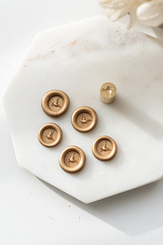 Set of five gold wax seals with dove design and matching mini stamp head on marble background