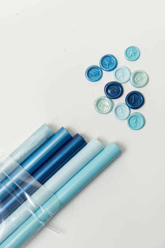 Coastal Breeze sealing wax sticks with a variety of blue wax seal impressions featuring starfish and seahorse designs for coastal stationery.