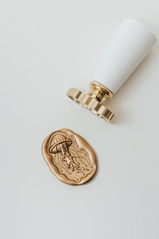 Gold jellyfish wax seal with a white wooden wax seal stamp on a clean white surface, perfect for coastal wedding invitations, letters, and creative paper crafts.