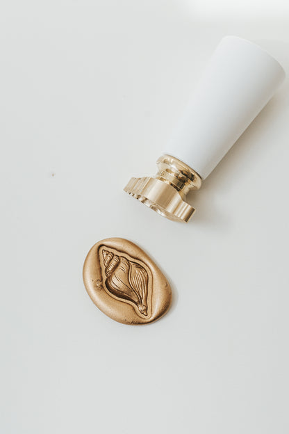 Finished conch shell wax seal beside a brass wax seal stamp for coastal wedding invitations and luxury stationery.