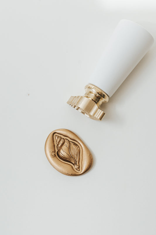 Finished conch shell wax seal beside a brass wax seal stamp for coastal wedding invitations and luxury stationery.