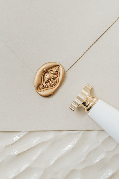 Close-up of a conch wax seal on an invitation with a brass wax seal stamp for coastal stationery and envelope sealing.