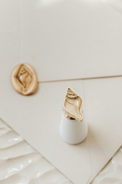 Conch brass wax seal stamp with a white handle featuring an engraved seashell design for coastal wedding invitations and stationery.
