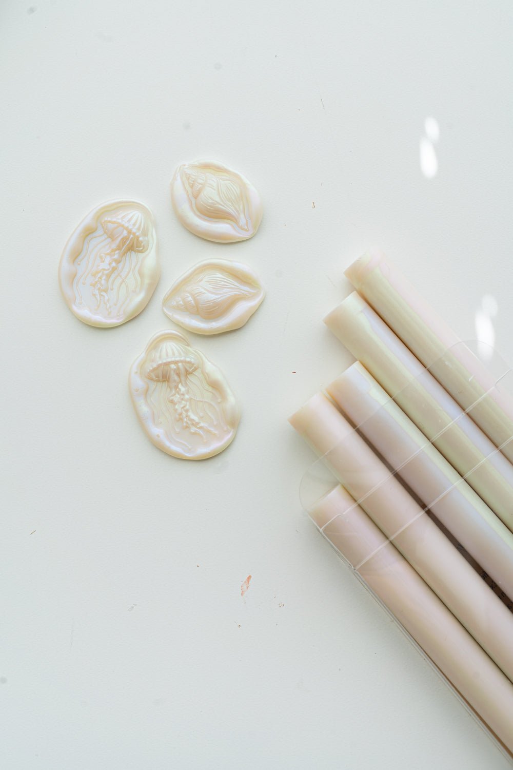 Mother-of-pearl sealing wax sticks with iridescent jellyfish and seashell wax seals on a white surface.