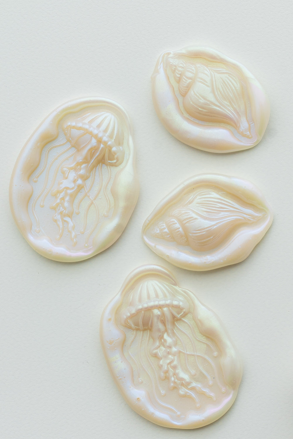 Iridescent mother-of-pearl wax seals featuring jellyfish and seashell designs on a soft white background.
