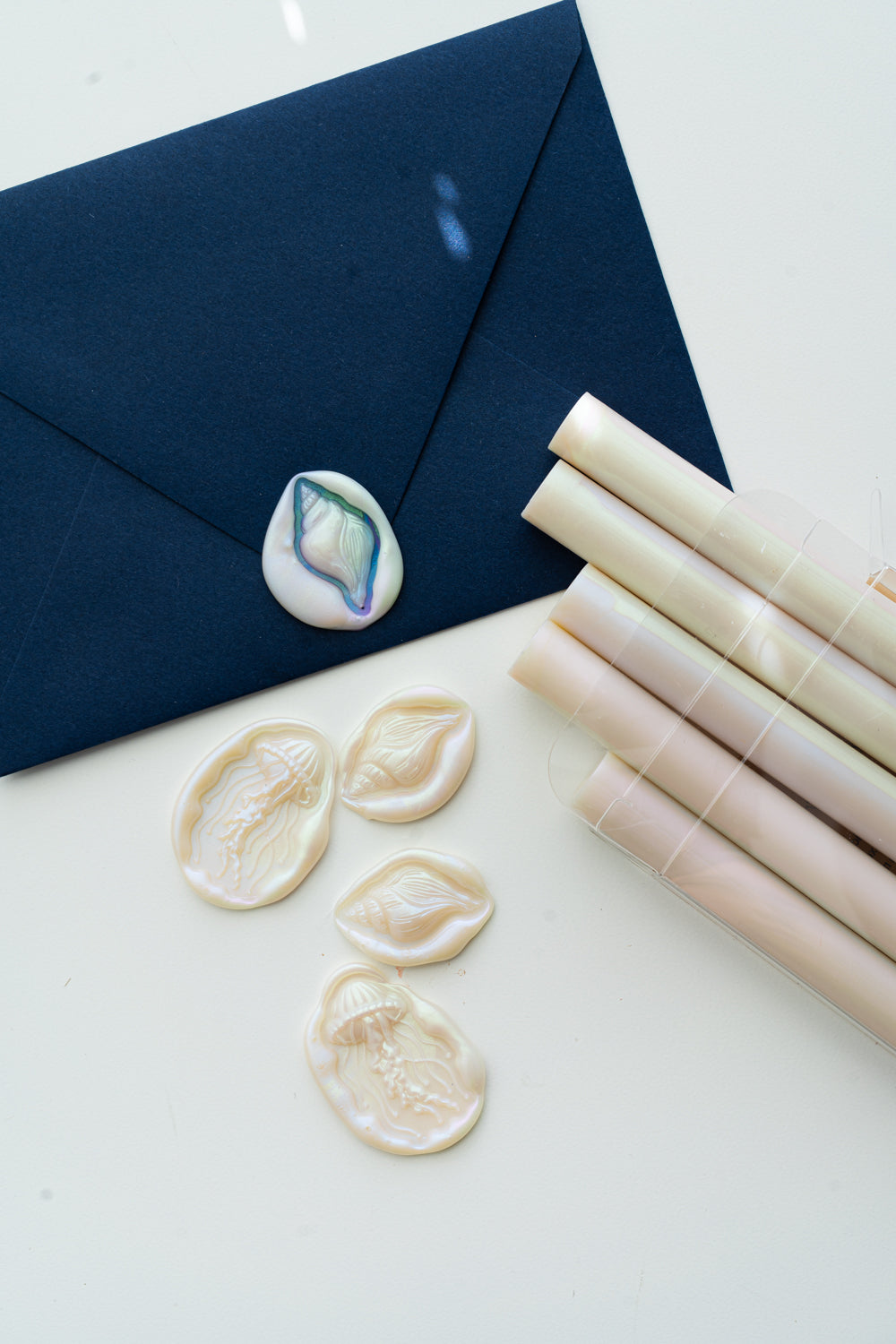 Navy envelope with an iridescent shell wax seal beside Mother-of-Pearl sealing wax sticks and ocean-inspired jellyfish and seashell wax seals.