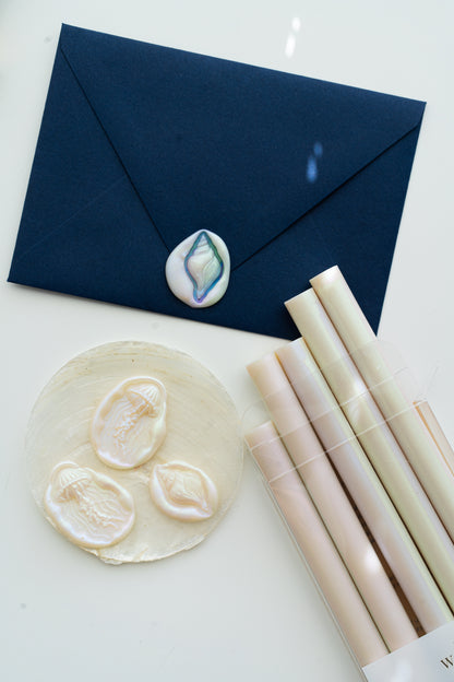 Mother-of-pearl sealing wax sticks, jellyfish and seashell wax seals, and a navy envelope sealed with an iridescent shell wax seal.