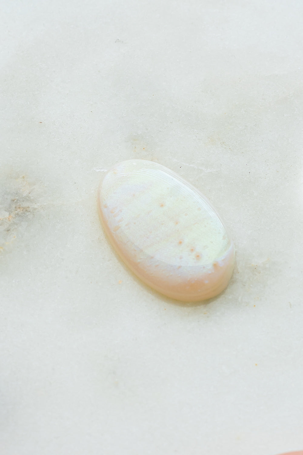 Close-up of an iridescent mother-of-pearl wax seal on a light stone surface.