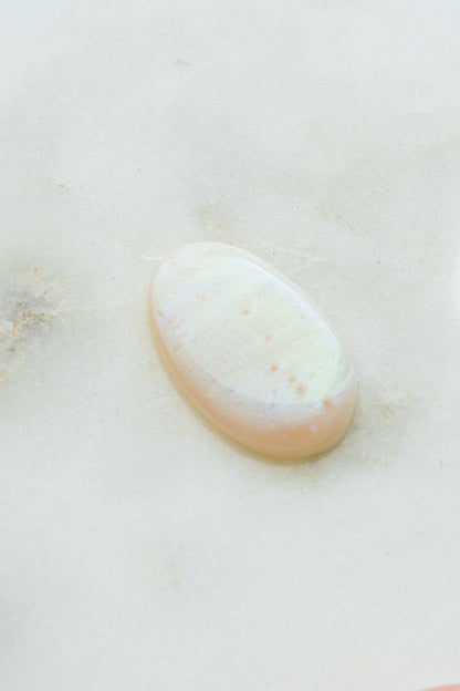 Close-up of an iridescent mother-of-pearl wax seal on a light stone surface.