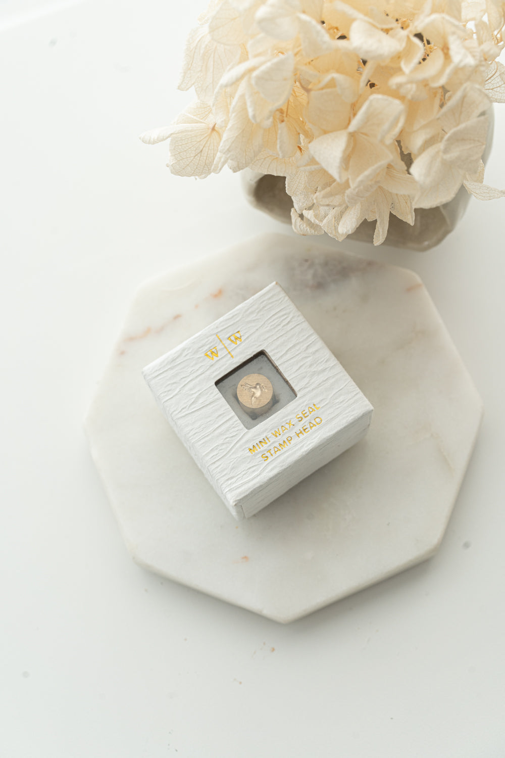 Mini wax seal stamp head in white textured box with gold foil text, styled with dried flowers on marble tray