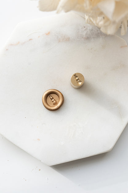 Brass mini wax seal stamp head with bunny design beside gold wax seal on marble surface
