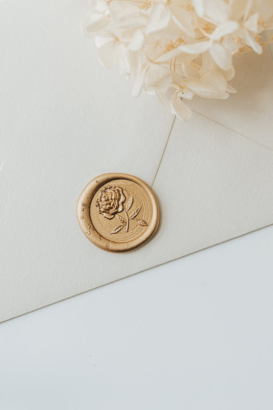 Gold peony wax seal on cream envelope with dried ivory hydrangea flowers and textured paper