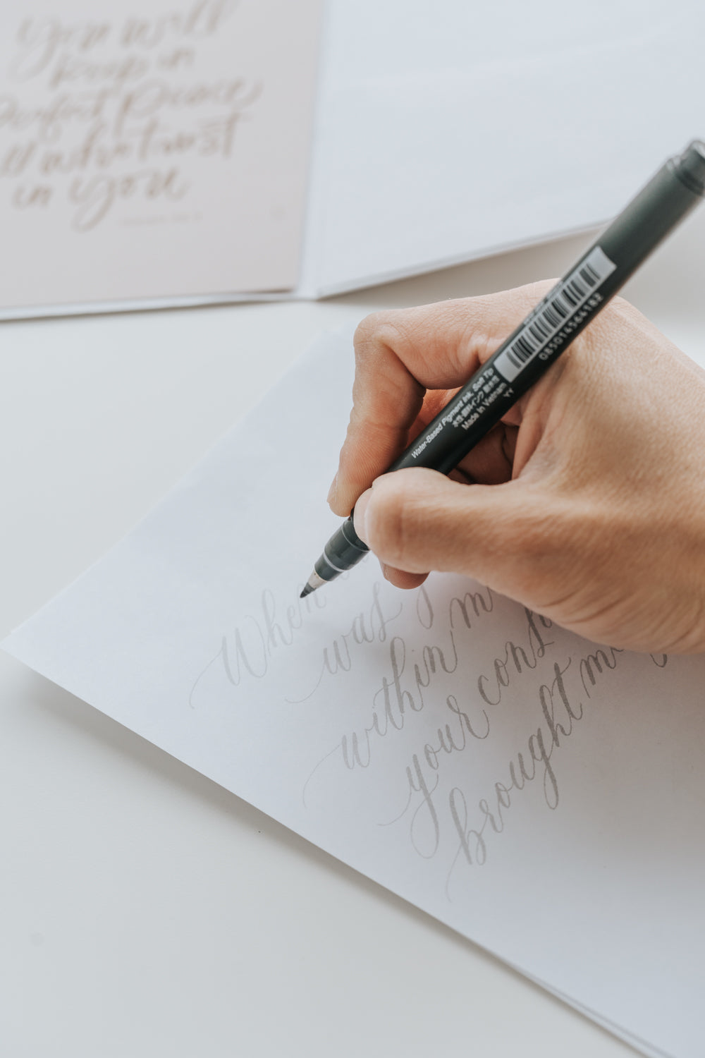 Writing calligraphy practice on tracing paper with pen, modern lettering workspace